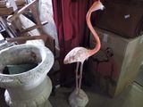 un flamant rose posé à côté d'une jardinière en béton