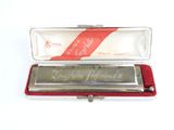 une image représentant un harmonica dans un étui, entouré d'un ruban rouge