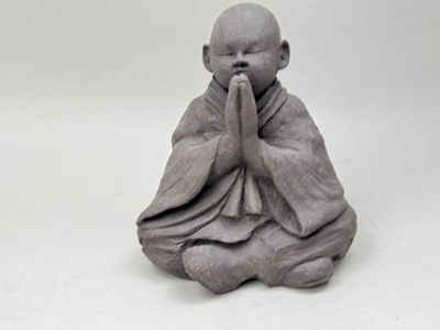 figurine de Bouddha assis sur une surface blanche, les mains devant la bouche
