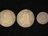 three silver coins are shown in a row on a black surface