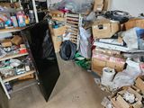 a black refrigerator in the middle of a cluttered room