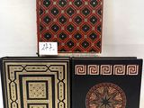 three books with designs on them sitting on a white surface