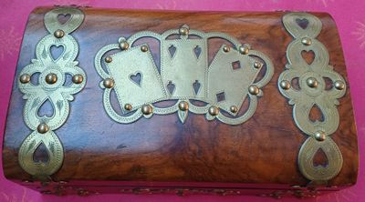 une boîte en bois ornée de décorations métalliques, posée sur un fond rose