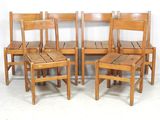 Quatre chaises en bois sont alignées contre un mur blanc.