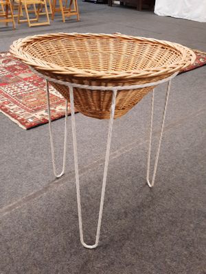 un panier en osier posé sur un support métallique au milieu d'une pièce