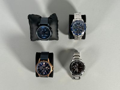 four different watches sitting on a white surface with a black bag