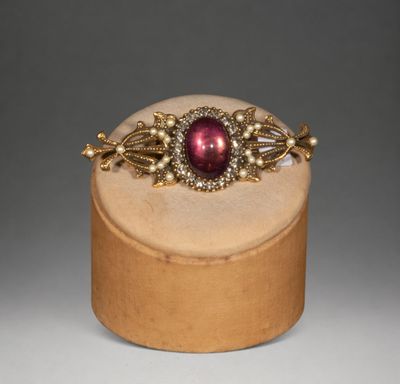 a close up of a gold and red broocher on a wooden stand