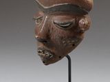 une photo d'une sculpture en bois représentant le visage d'un homme, posée sur un socle