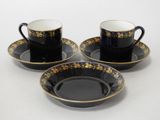 three black and gold coffee cups and saucers on a white surface