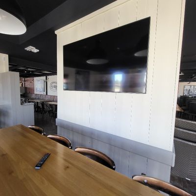 des tables et des chaises dans une pièce où est accrochée une télévision à écran plat au mur