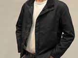 un homme debout, vêtu d'une veste noire et d'un jean