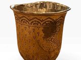 a gold cup with a design on it on a white surface