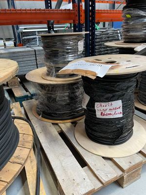 de nombreuses bobines de fils noirs posées sur des palettes dans un entrepôt