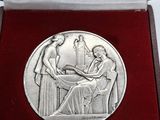 une image représentant une médaille d'argent dans un coffret rouge orné de la photo d'une femme assise à une table