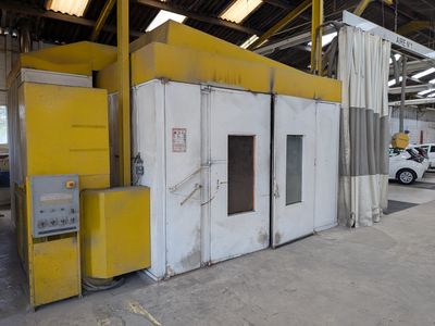 une machine jaune et blanche dans un entrepôt, avec une voiture blanche en arrière-plan