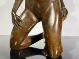 bronze statue of a naked woman sitting on a black surface