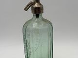 an old green glass bottle with a metal stopper on a white surface