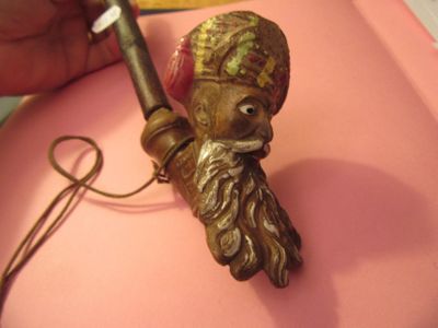 une figurine en bronze représentant un homme barbu coiffé d'un chapeau, posée sur un fond rose
