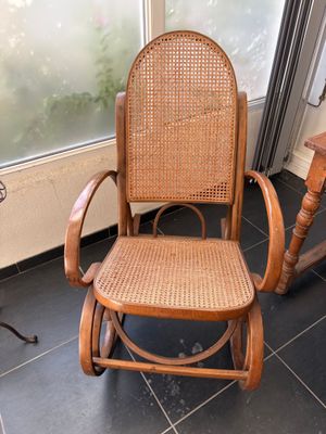 un fauteuil à bascule en bois avec une assise en osier, placé devant une fenêtre