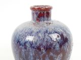 un vase bleu et rouge posé sur une surface blanche