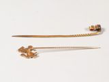 two gold pins with a flower on them on a white surface