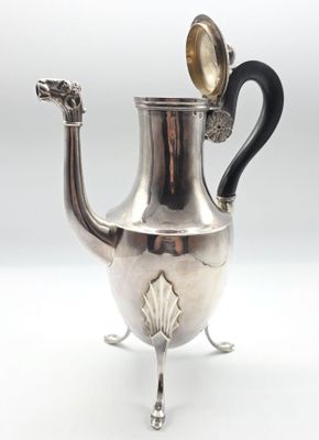une théière ancienne en argent, dotée d'une anse noire et posée sur un socle