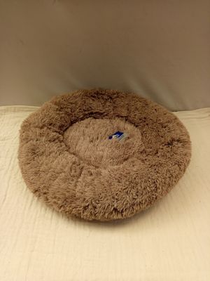 un panier pour chien marron posé sur un lit recouvert d'un drap blanc