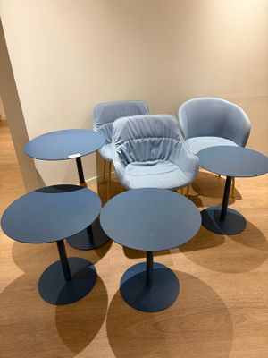 Plusieurs chaises et tables bleues sont disposées en cercle sur un parquet.