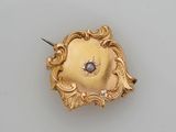 une broche en or 18 carats ornée d'une pierre bleue au centre