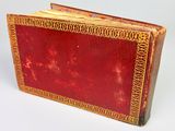 an old red book with gold trim sitting on top of a white surface