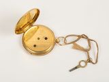an antique pocket watch with a key on a white surface