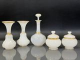 Plusieurs vases blancs ornés de bordures dorées sont alignés sur un fond noir.