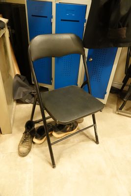 a black folding chair in a room with blue lockers