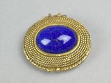 a close up of a blue and gold broochle on a white surface