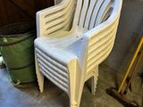 a white plastic chair sitting in a garage next to a trash can