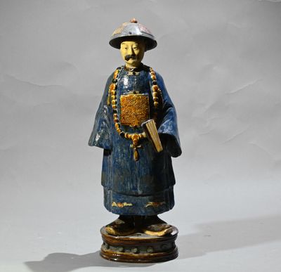 une statue en bois représentant un homme coiffé d'un chapeau et tenant un livre