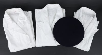 trois paires de pantalons blancs et un chapeau noir posés sur une surface noire
