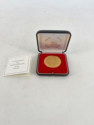 une photo d'une médaille d'or dans un écrin rouge, accompagnée d'un certificat