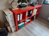 a red book shelf in the corner of a room