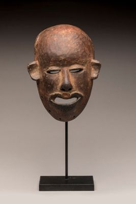 un masque en bois posé sur un socle noir, devant un fond blanc