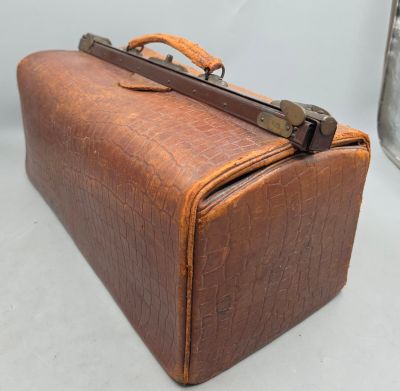 une valise en cuir marron posée sur une surface blanche, à côté d'un conteneur métallique