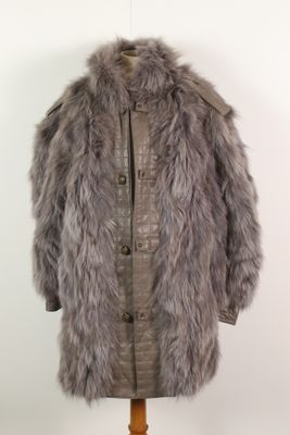 un manteau de fourrure gris posé sur un mannequin, devant un mur blanc
