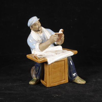a figurine of a man sitting at a desk reading a book