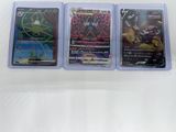 trois cartes Pokémon différentes, rangées dans des pochettes en plastique, posées sur une surface blanche