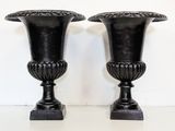 two black vases sitting on a table with a white wall in the background