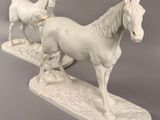 pair of white porcelain horses standing on top of a white base