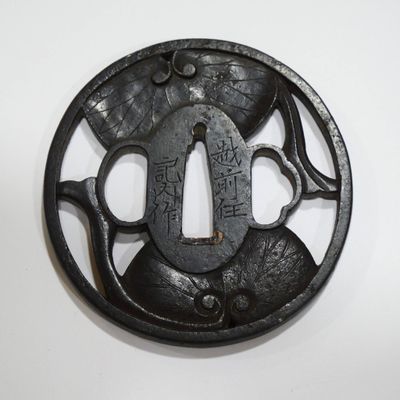 une tsuba en fer noir comportant une inscription sur un fond blanc