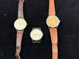 Trois montres différentes sont exposées dans une vitrine posée sur une table.