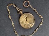 une montre de poche en or, suspendue à une chaîne, posée sur une table