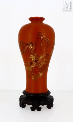 un vase rouge orné de feuilles dorées, posé sur un socle